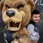 Ernesto Duran-Gutierrez, holding a First Generation Oakland University button, posing with the Grizz bear mascot.